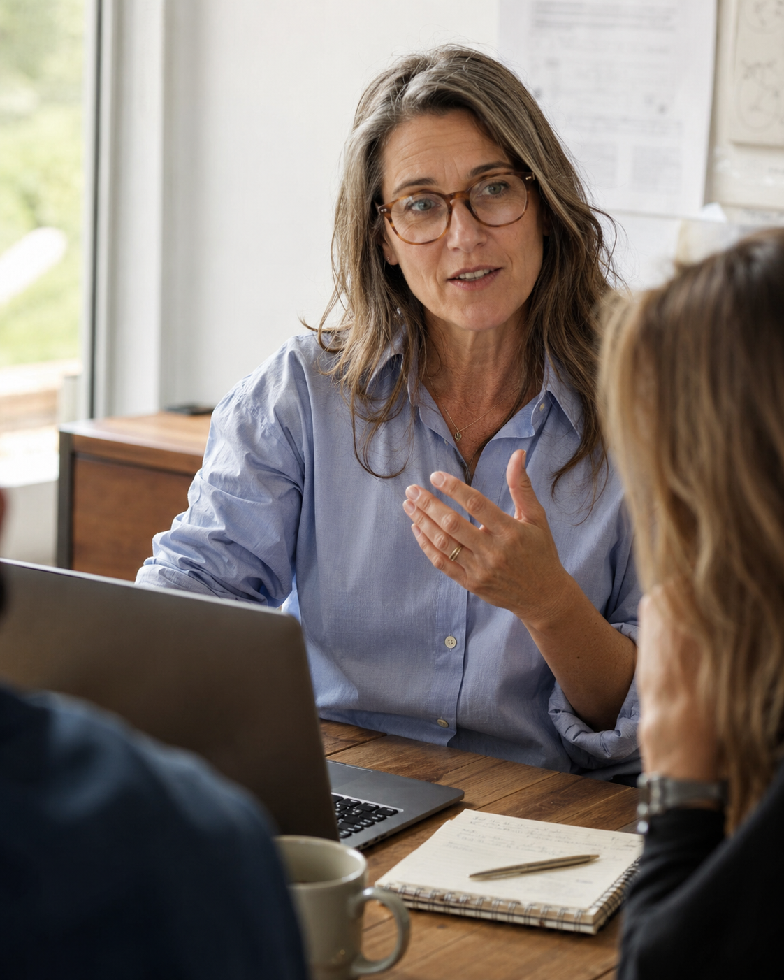 Photograph a woman aged 45-55 leading a normal work meeting in soft daylight, mid-conversation and visibly at ease, with no product in frame. The image is here to make the desired outcome—trusting her mind and having energy left after work—feel specific rather than aspirational.